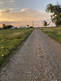 Empty road amidst field against sky