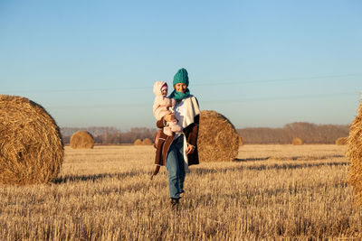 A young mother playing her daughter and enjoying nature on the back of a background of autumn field 