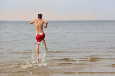Rear view of shirtless man standing at beach against sky