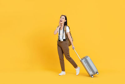 Woman with umbrella standing against yellow background