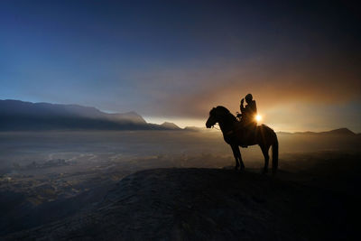 Silhouette man sitting on horse over mountain