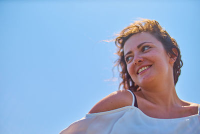 Low angle portrait of young woman against clear blue sky