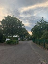 Empty road by trees in city against sky