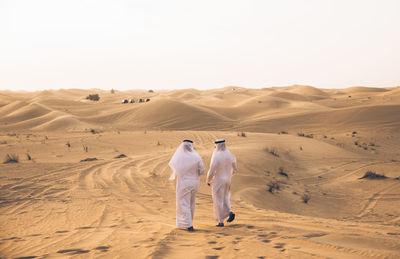 Rear view of men walking in desert against sky