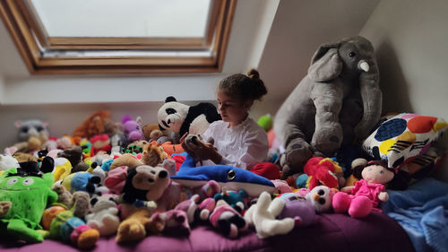 Little girl playing surrounded by her stuffed animals in bed