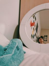 Woman looking on her reflection in the mirror on bed at home