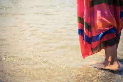 Low section of woman standing in water at lakeshore