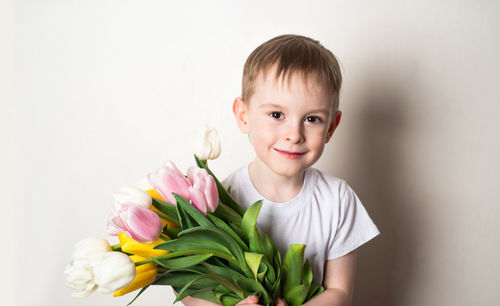 Portrait of a smiling boy with freckles in t-shirt with a bouquet of tulips on a white background