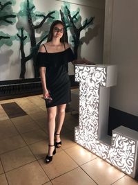 Portrait of teenage girl standing by illuminated alphabet l on tiled floor