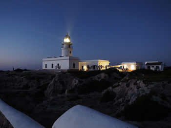 Lighthouse amidst buildings against clear sky at dusk
