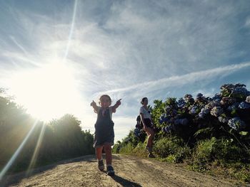 Preschool boy gesturing against woman on dirt road during sunny day