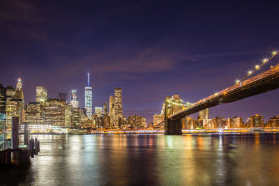 Illuminated bridge over river with buildings in background at night