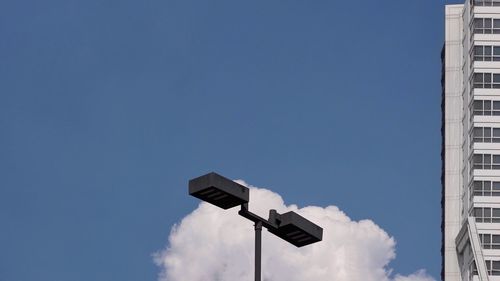 Black electric street light pole with white condominium building and white cloud.