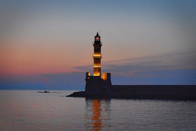 Lighthouse by sea against sky during sunset