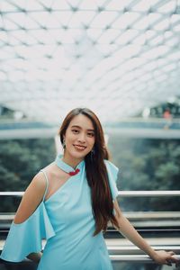 Portrait of smiling young woman standing against railing outdoors