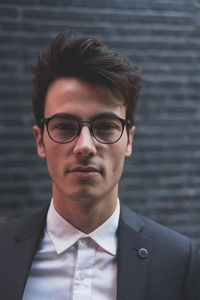 Close-up portrait of young businessman wearing eyeglasses against wall