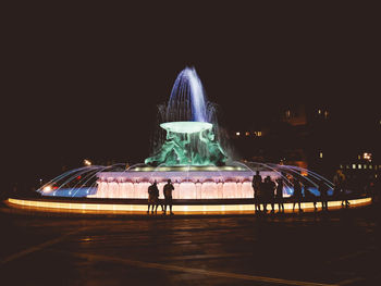 People at illuminated city against sky at night