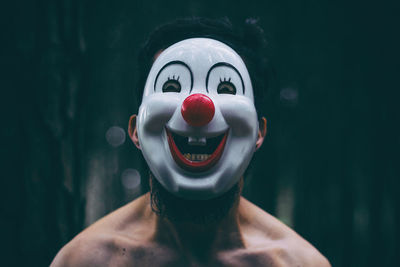 Portrait of shirtless mid adult man wearing clown mask while standing outdoors