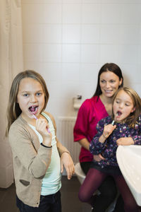 Portrait of girl brushing teeth with mother and daughter in bathroom