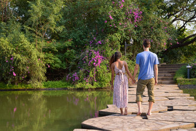 Rear view of friends standing by lake against trees