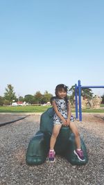 Portrait of happy woman sitting in park against clear sky