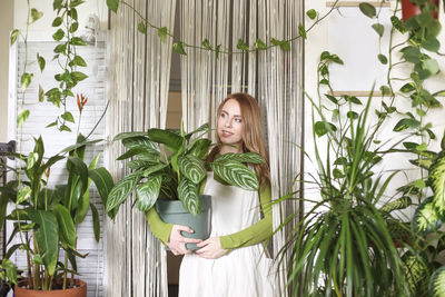 Young woman standing against potted plants