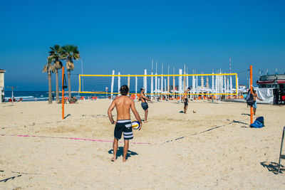 People on beach against clear blue sky