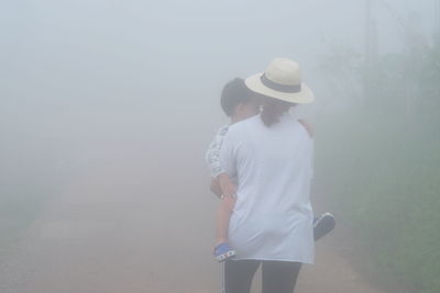 Rear view of woman carrying son on footpath during foggy weather