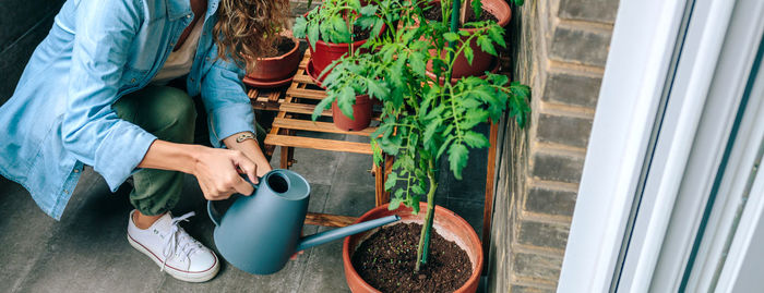 Woman using watering can with plants of urban garden on terrace