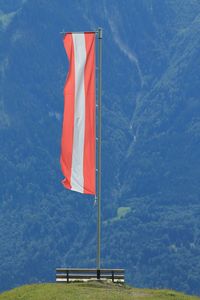 Flag on austria by bench on peak against mountain