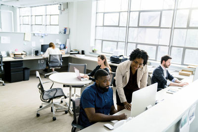 Businesswoman standing by colleague using desktop computer