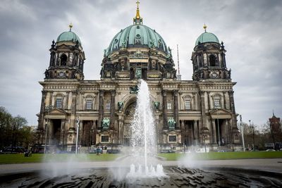 Fountain in city against cloudy sky