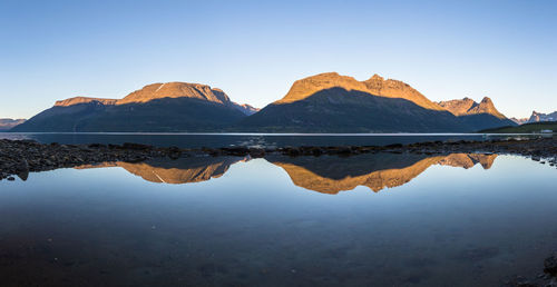 Reflection of rocky mountains on calm lake against clear sky