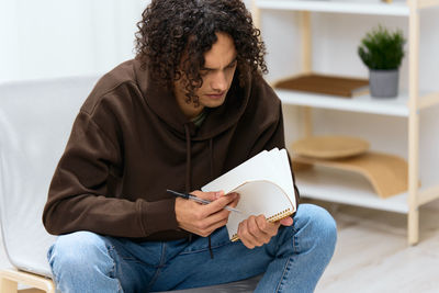 Young man reading book while sitting on sofa at home