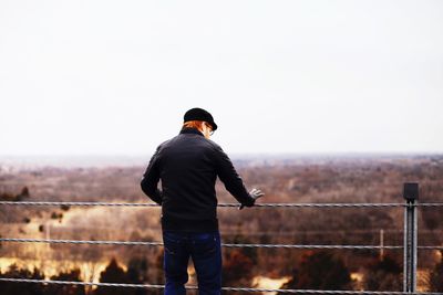 Rear view of man standing by railing against clear sky