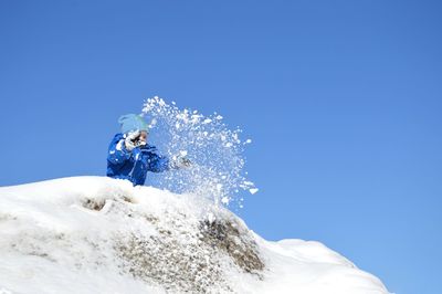 Low angle view of boy playing with snow against clear blue sky