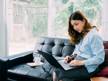 Young woman using mobile phone while sitting on sofa at home