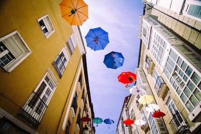 Low angle view of umbrellas hanging amidst buildings in city against sky