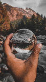 Cropped image of hand holding crystal ball against rock