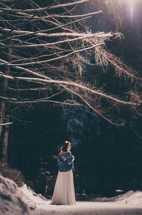 Full length of young woman standing by trees in forest