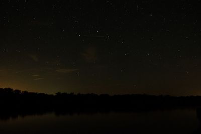 Silhouette trees on landscape against sky at night