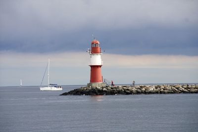 Lighthouse by sea against cloudy sky