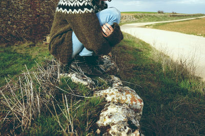 Low section of young woman hugging knees while crouching on field