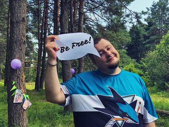 Young man holding be free speech bubble against trees