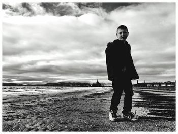 Boy standing at beach against cloudy sky