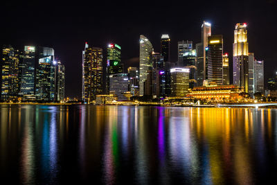 Illuminated buildings by river against sky at night