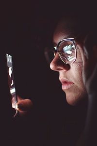 Close-up of woman wearing eyeglasses using smart phone in darkroom