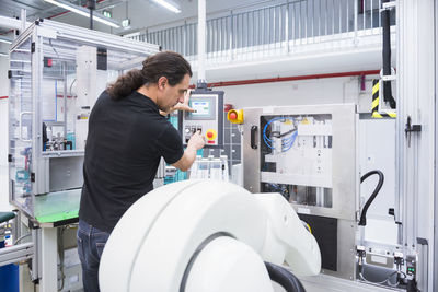 Man operating assembly robot in factory