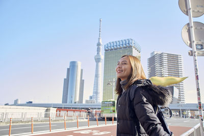 Young woman smiling while standing in city against clear sky