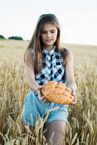 Teenager girl holding loaf of bread while standing amidst farm